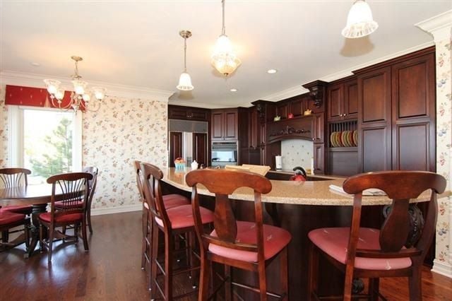 Kitchen with dark cherry cabinets, granite island seating, hardwood floors, and an adjoining dining area.