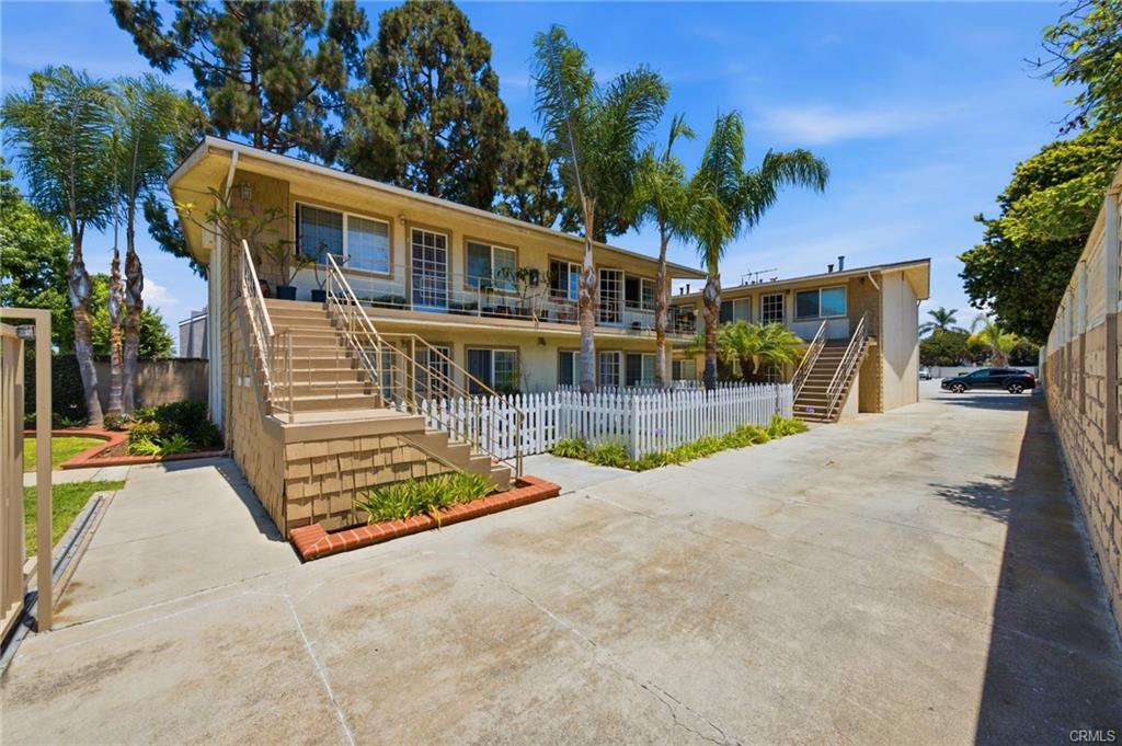 Two-story multifamily building with balconies, exterior stairs, and a wide concrete driveway.