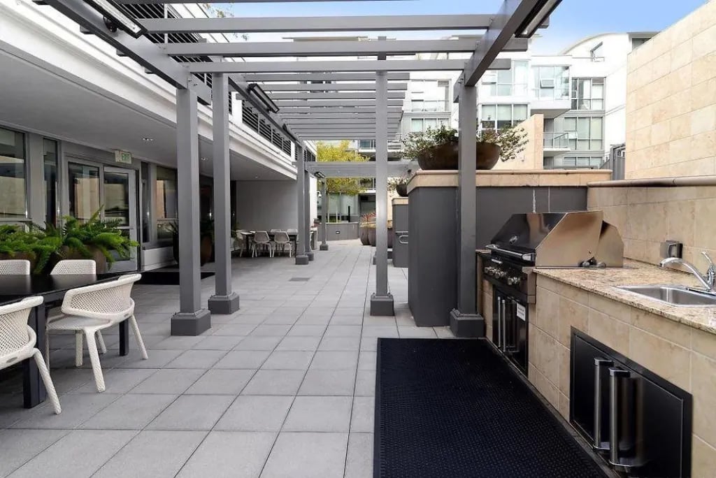 An outdoor patio area at the Madrone, featuring a grill station, sink, and a large dining table under a modern pergola.