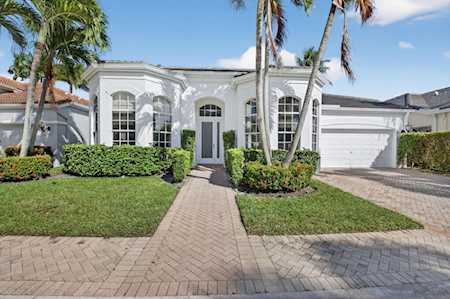 White home with arched windows, palm trees, and a brick driveway.