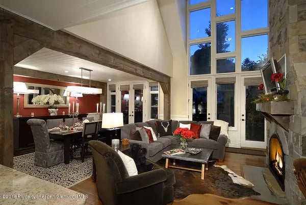 Living room with a gray sectional, vaulted windows, and a stone fireplace beside the dining area.