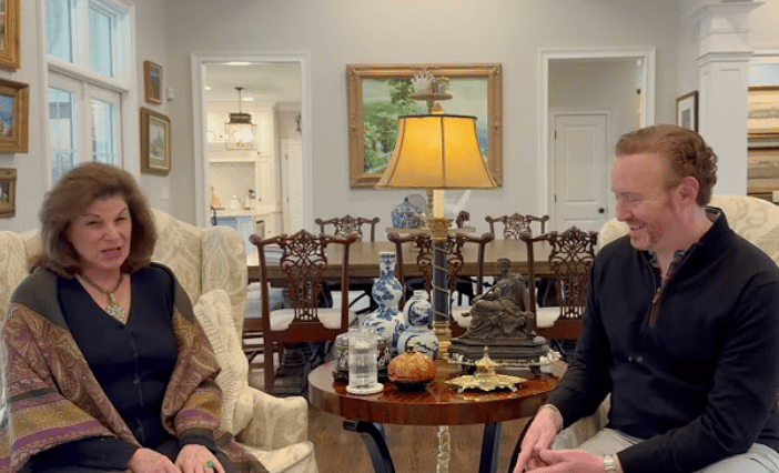A woman and man converse in a formal dining room beside a set table.