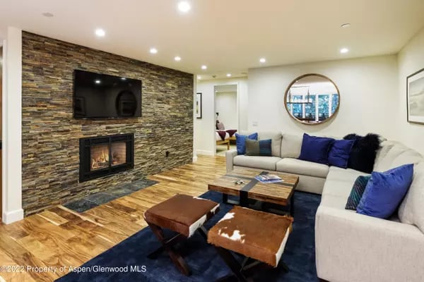 Living room with a stone fireplace wall, mounted television, sectional sofa, and wood flooring.