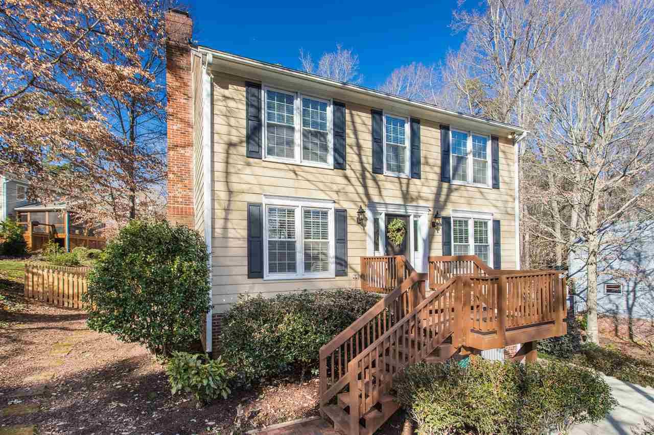 Two-story beige house with dark shutters and a raised wooden deck and stairs.