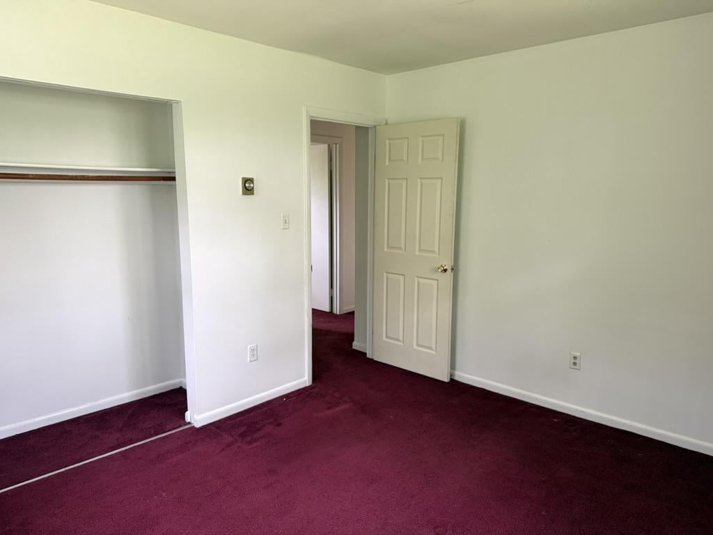 Empty bedroom with burgundy carpet, a built-in closet, and an open door.