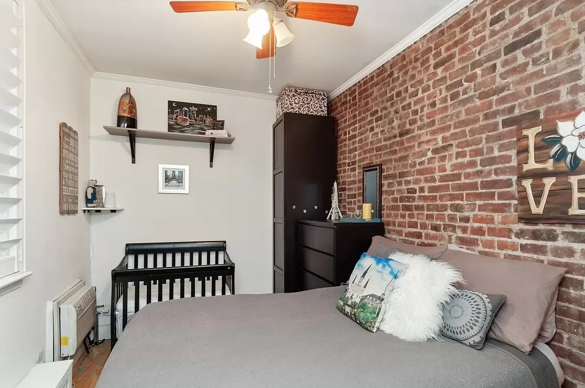 Bedroom with an exposed brick wall, large bed, and black crib.