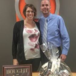 Jason and Jenn celebrate their home purchase beside a bought sign and gift basket.