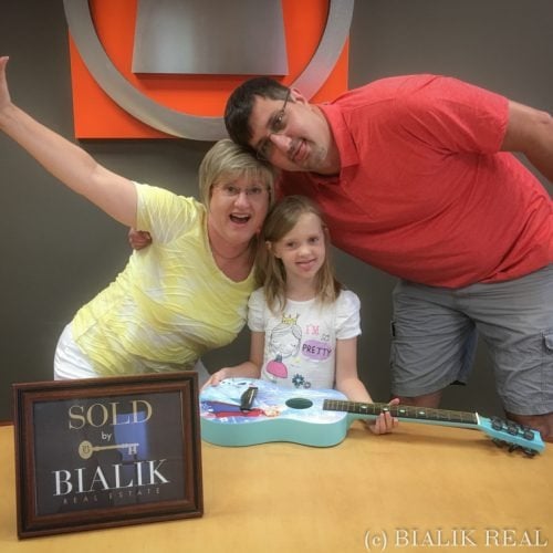 Greg and Allie celebrate their home closing with their daughter beside a Bialik Real Estate sold sign.