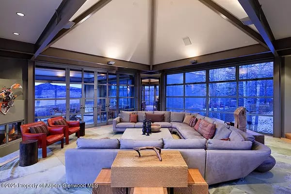 Living room with vaulted ceiling, sectional sofa, and expansive windows overlooking snowy mountain scenery.
