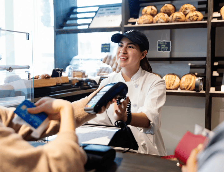 Bakery employee takes a customer's payment at the counter, with pastries displayed behind her.