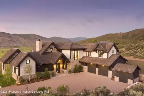 Large mountain home with multiple gabled roofs, stone accents, and a detached garage beneath a dusky sky.