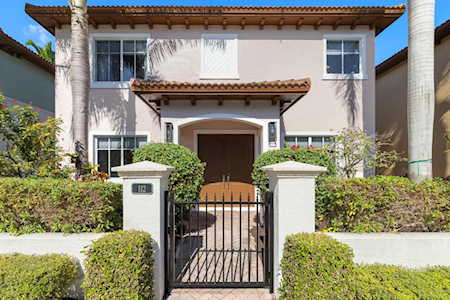 Two-story stucco home with a tiled entry roof, black gate, and trimmed hedges.