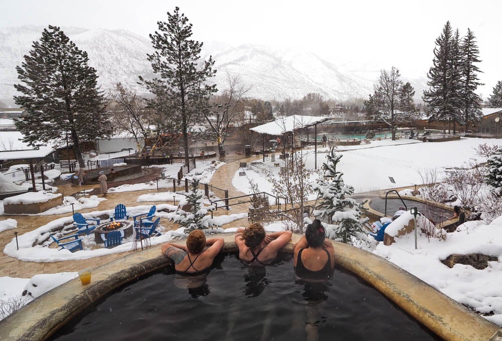 People soak in an outdoor hot spring surrounded by snow and mountain scenery.