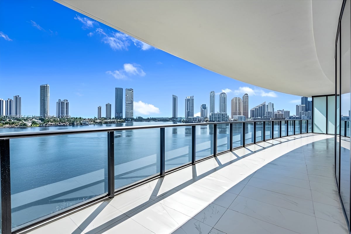 High-rise balcony overlooking blue water and a distant skyline, with glass railings and white tile flooring.