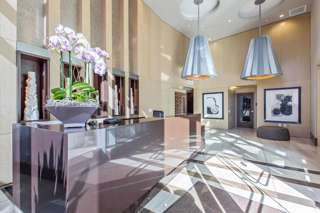 Arden Residences sophisticated lobby concierge area with polished stone reception desk, orchid arrangements, pendant lighting, and elevator bank in Mission Bay San Francisco