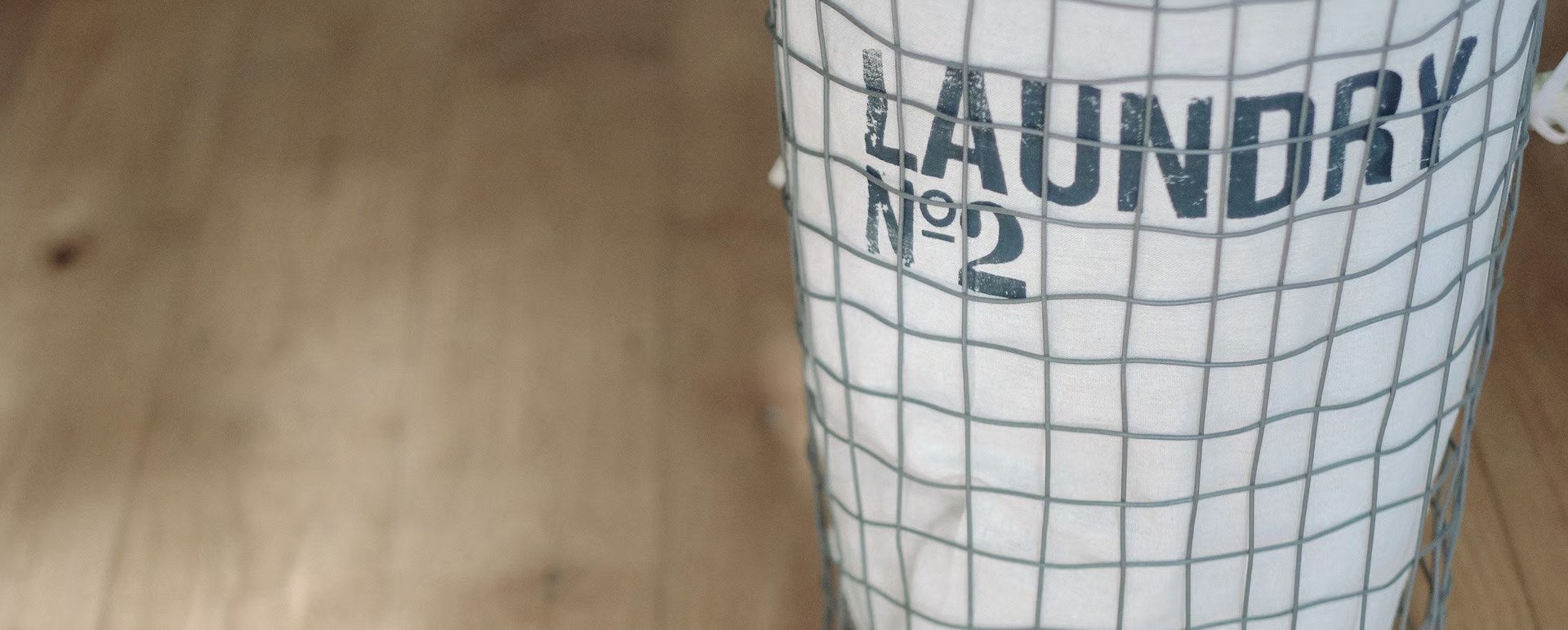 White fabric laundry hamper with a gray wire grid and “LAUNDRY” lettering.