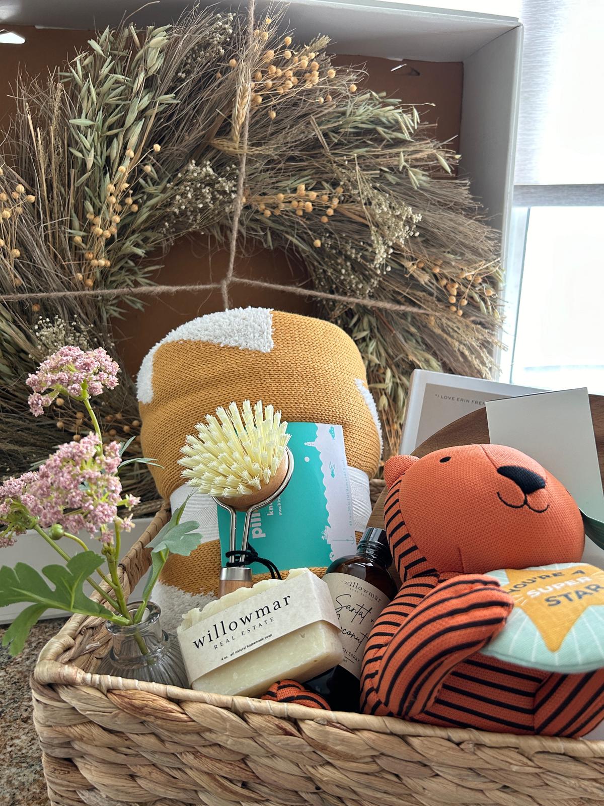 A woven basket of Willowmar Real Estate gifts, including branded soap and an orange tiger plush.