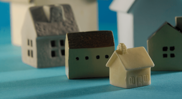 Small ceramic houses sit on a blue surface, with soft lighting creating a warm, inviting atmosphere. A cream-colored house is in the foreground.