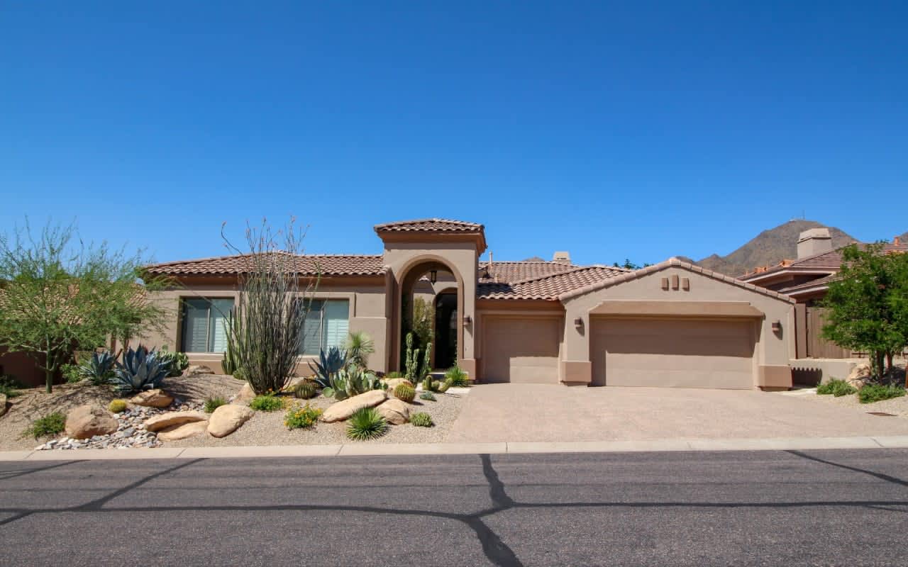 Desert-inspired luxury home with terracotta roof, arched entry, and stone landscaping, ideal for a tranquil oasis.