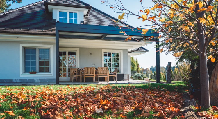 Home exterior with a covered patio, pergola, and autumn leaves across the lawn.