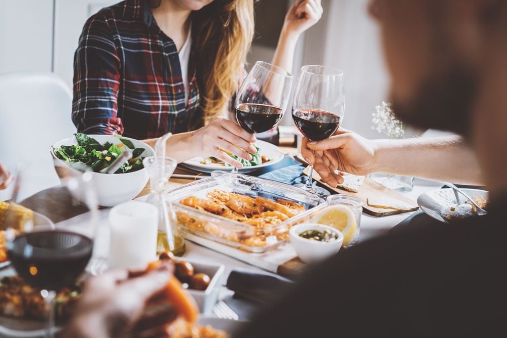 People toast with red wine over a table of shared dishes.
