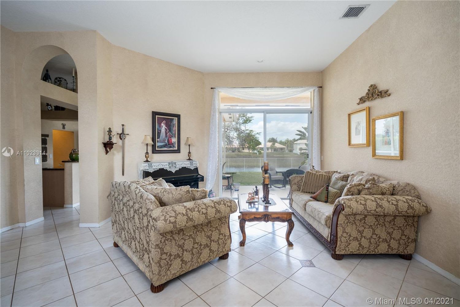 Furnished living room with patterned seating, tile floors, and sliding doors overlooking a canal.