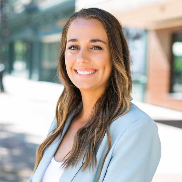 Ashlee Aplin, a real estate agent from the Insiders Realty, stands on a sidewalk wearing a blue blazer and white shirt.