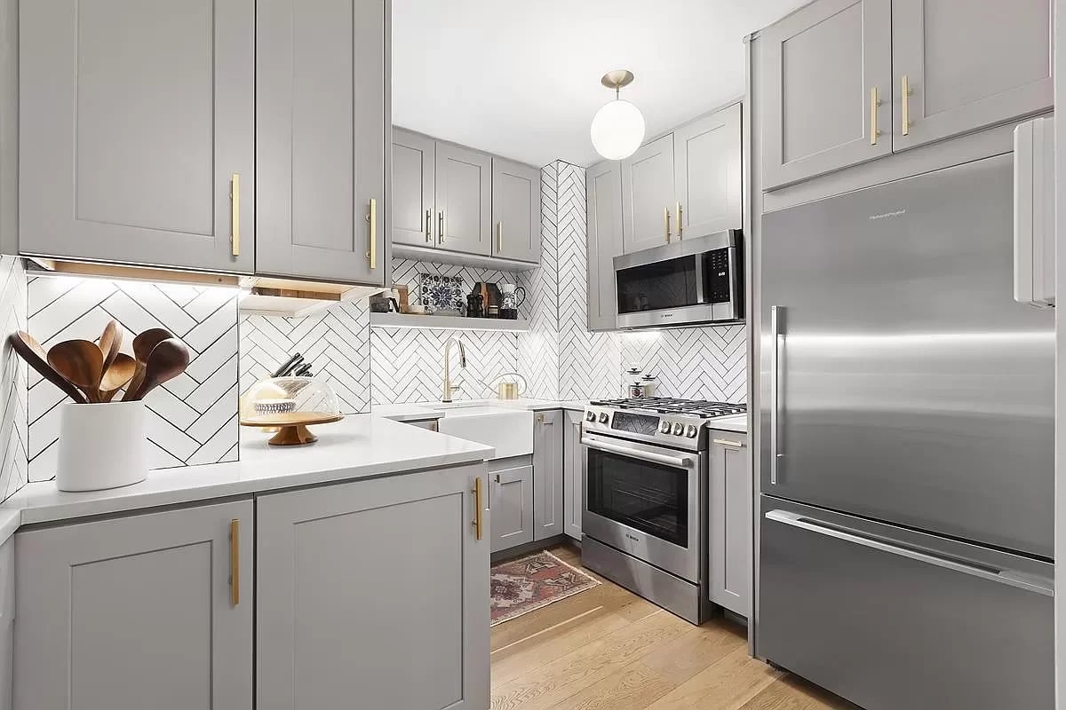 Renovated kitchen with gray cabinets, brass hardware, herringbone tile, and stainless steel appliances.