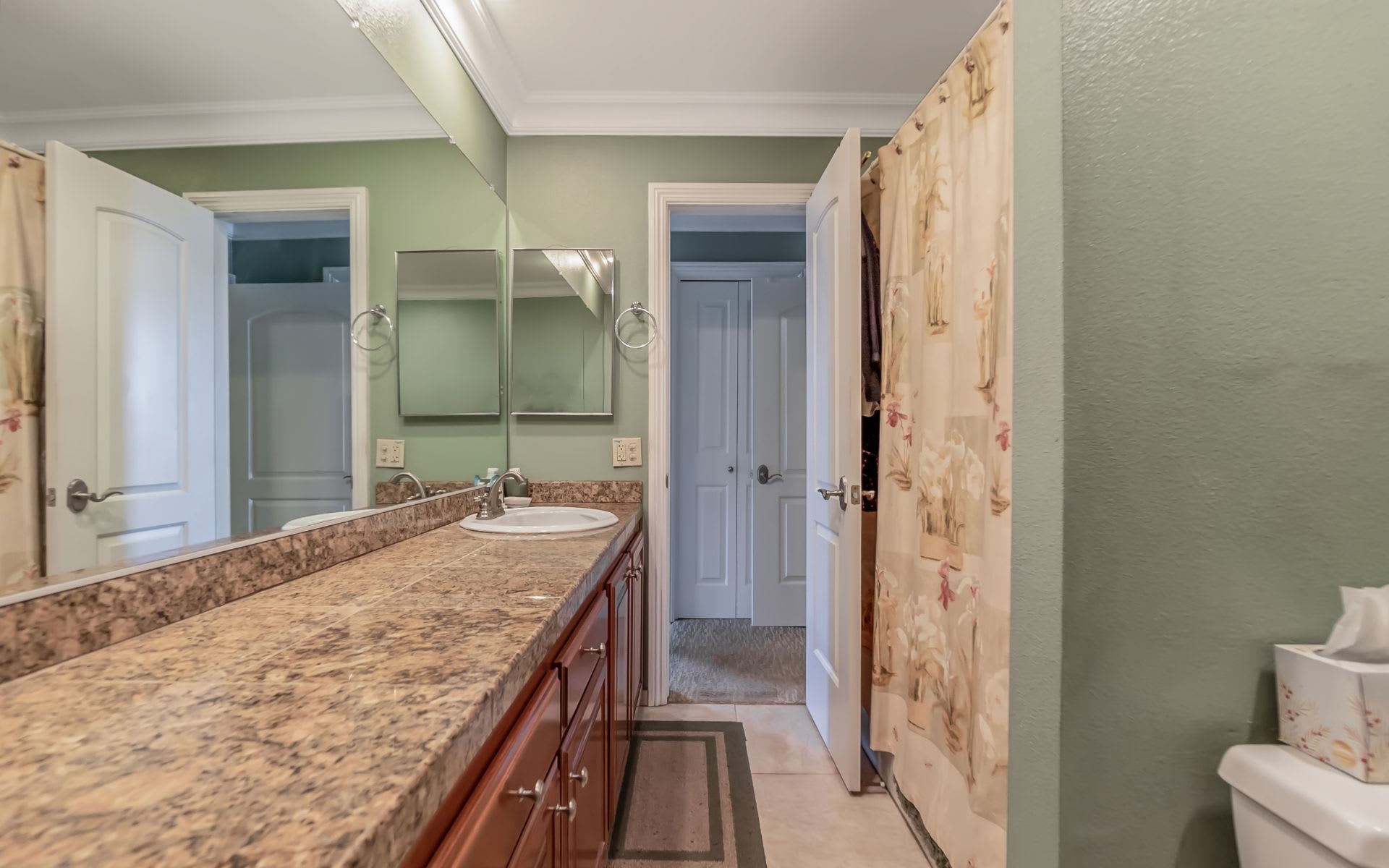 Bathroom with a long vanity, granite-pattern counter, large mirror, and floral shower curtain.