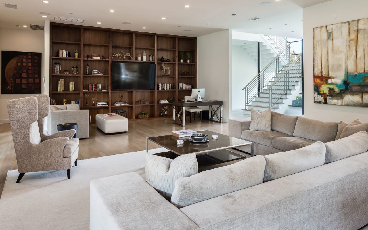 Airy living room with comfortable white couches, facing a striking wood wall with abundant shelving and centrally placed TV.