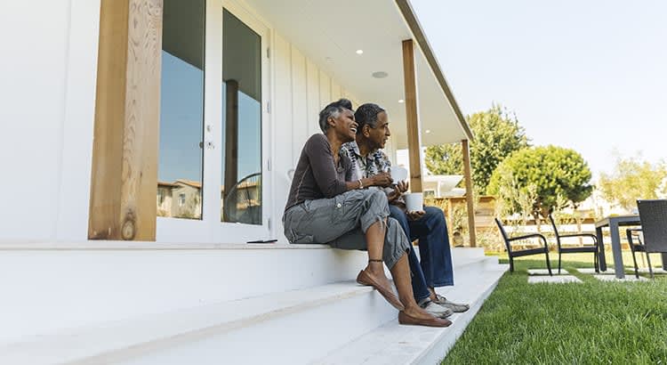 A relaxed couple is sitting on the porch of a house, symbolizing homeownership or outdoor leisure.