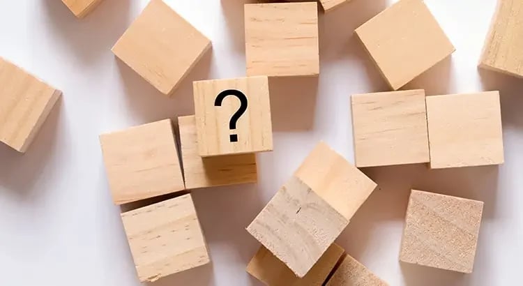 Wooden blocks arranged in a pattern with a question mark on one of the blocks, symbolizing uncertainty or decision-making.