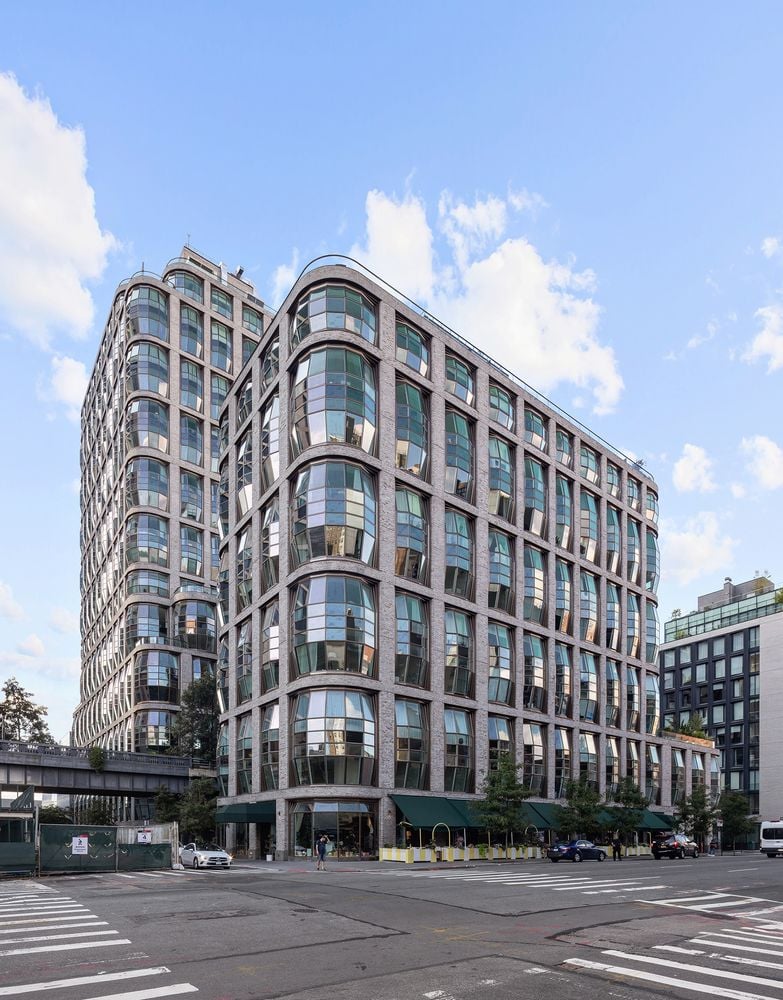 Modern residential building with a curved corner and large glass windows on a city street.
