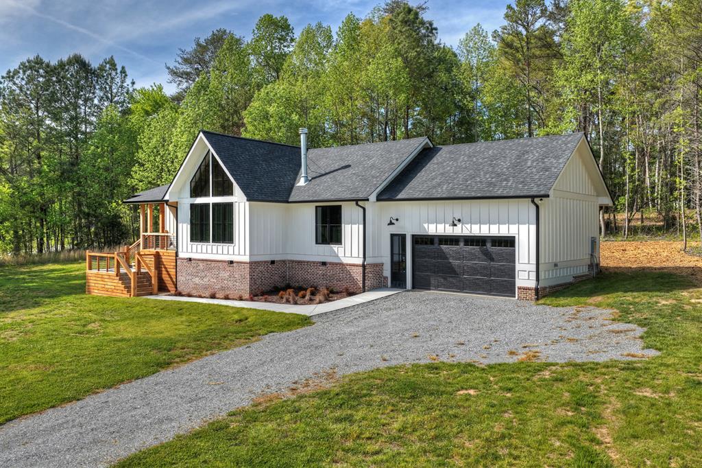 Modern farmhouse with white siding, brick foundation, and an attached garage beside a gravel driveway.