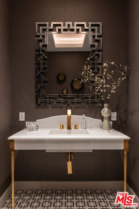 Powder room vanity with geometric mirror, brass fixtures, and patterned tile floor.