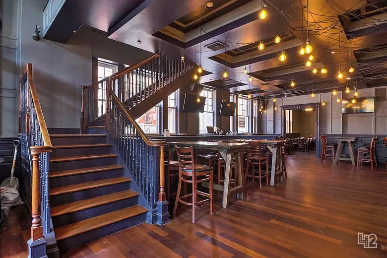Restaurant interior with a dark wood staircase, communal tables, and glowing pendant lights.