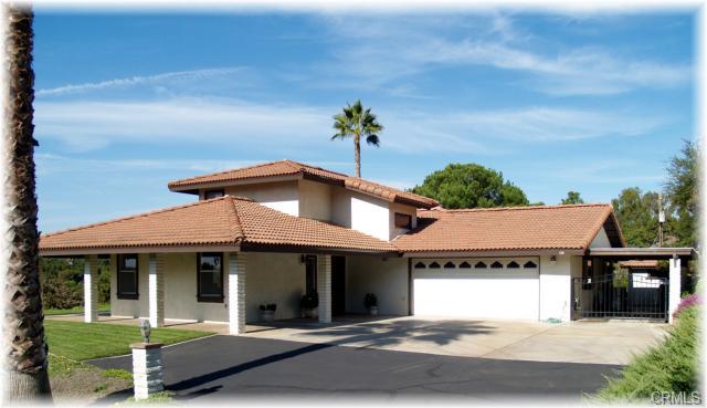 Home with a red tile roof, attached garage, and gated entrance beneath palm trees.