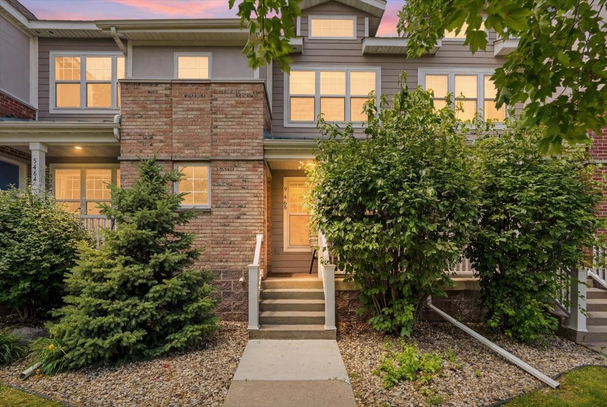 Front exterior of 5462 Coachman Place, a brick and vinyl townhouse in the Hatchery Hill neighborhood of Fitchburg, WI, shown at dusk with a private entry and landscaped walkway.