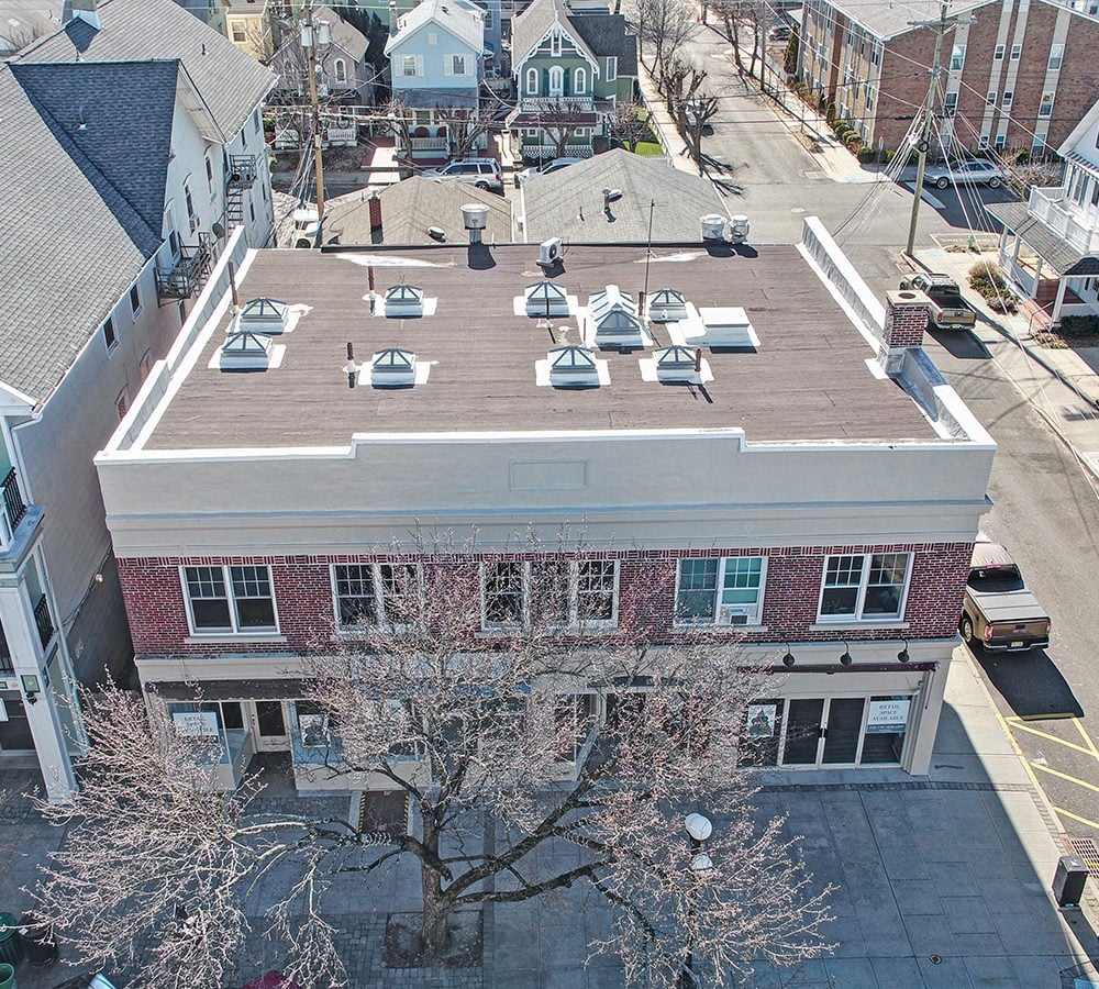 Two-story brick commercial building with a flat skylit roof and storefronts, viewed from above.