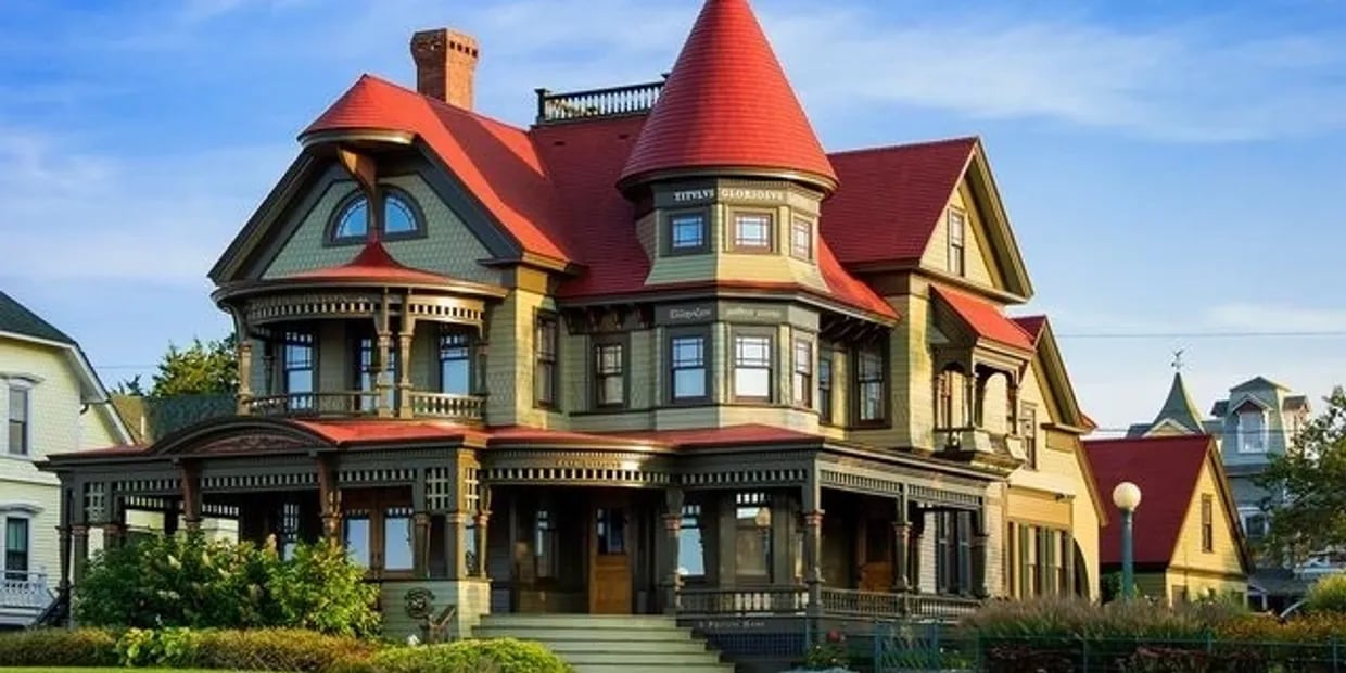 Queen Anne Victorian home with a conical turret, red roofs, and ornate wraparound porch.