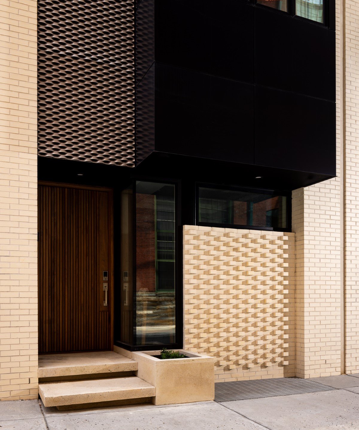 Modern home entrance with a dark wood door, sculptural brick screen, and black cladding.