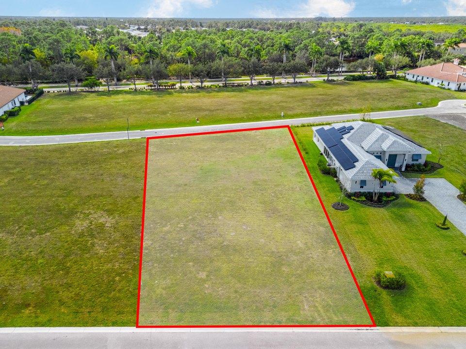 Vacant grassy lot outlined in red, between two roads beside a neighboring house.
