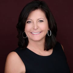 Woman with shoulder-length dark hair smiling in a black top and silver hoop earrings.