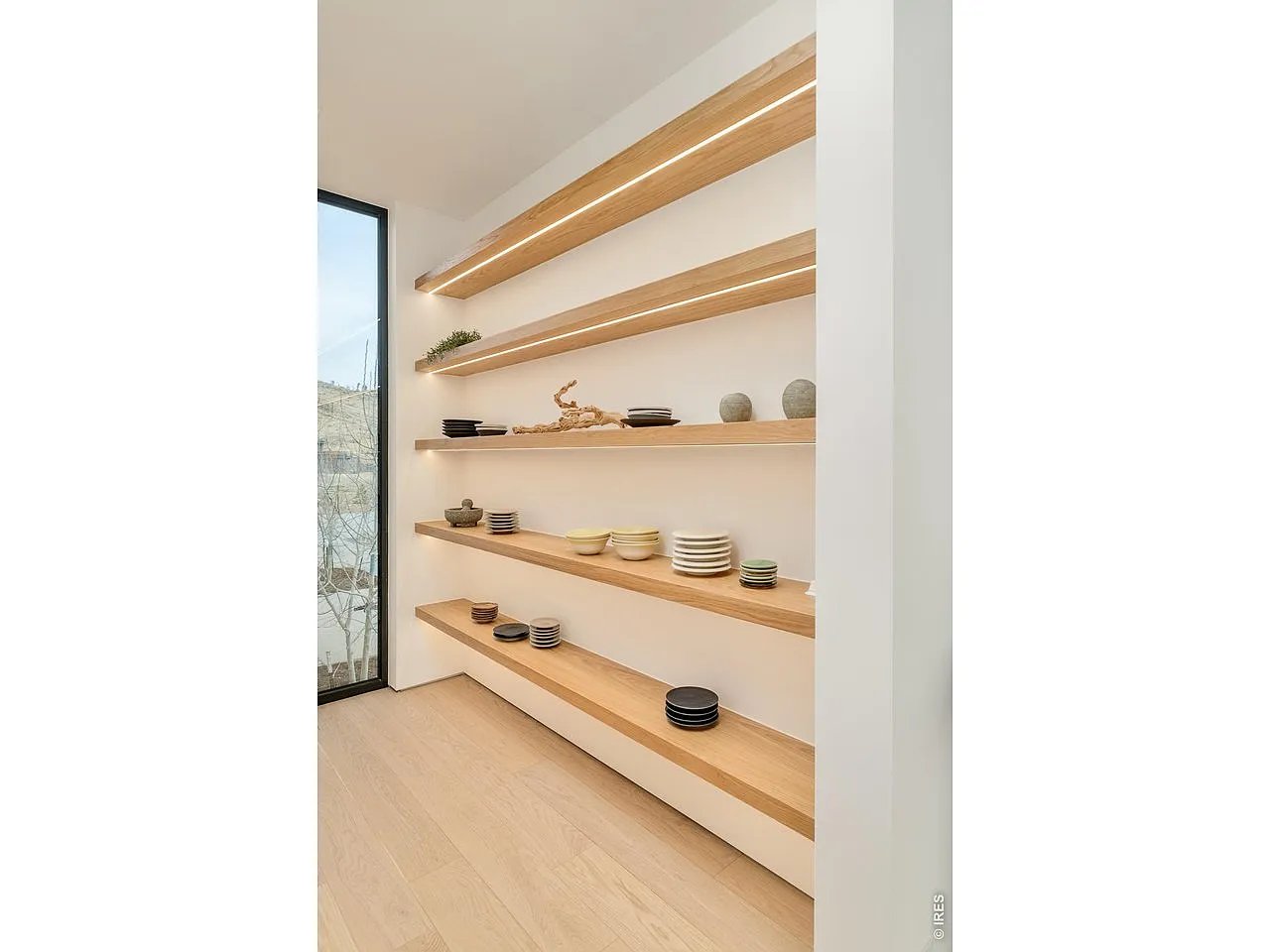 Built-in wood shelves display ceramic dishes beside a tall window.