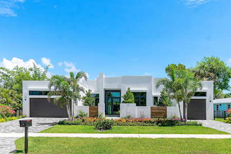 Modern white home with a broad driveway, palm trees, and a landscaped front lawn.