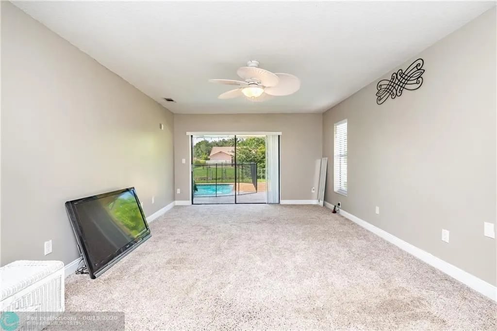 Living room with beige carpet, a ceiling fan, and sliding doors facing a pool.