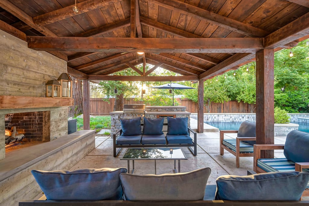 Covered patio with a wood-beam ceiling, stone fireplace, and poolside seating.