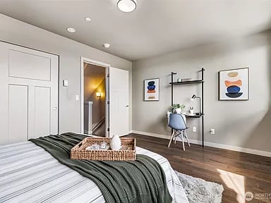 Staged bedroom with a dark green throw, woven bed tray, and sunlight on wood floors.
