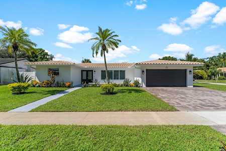 Single-story home with a dark garage door, broad front lawn, paved driveway, and palm trees.