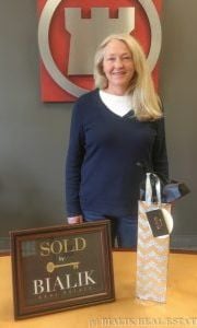 Nelly celebrating her closing beside a SOLD BY BIALIK plaque and a patterned gift bag.